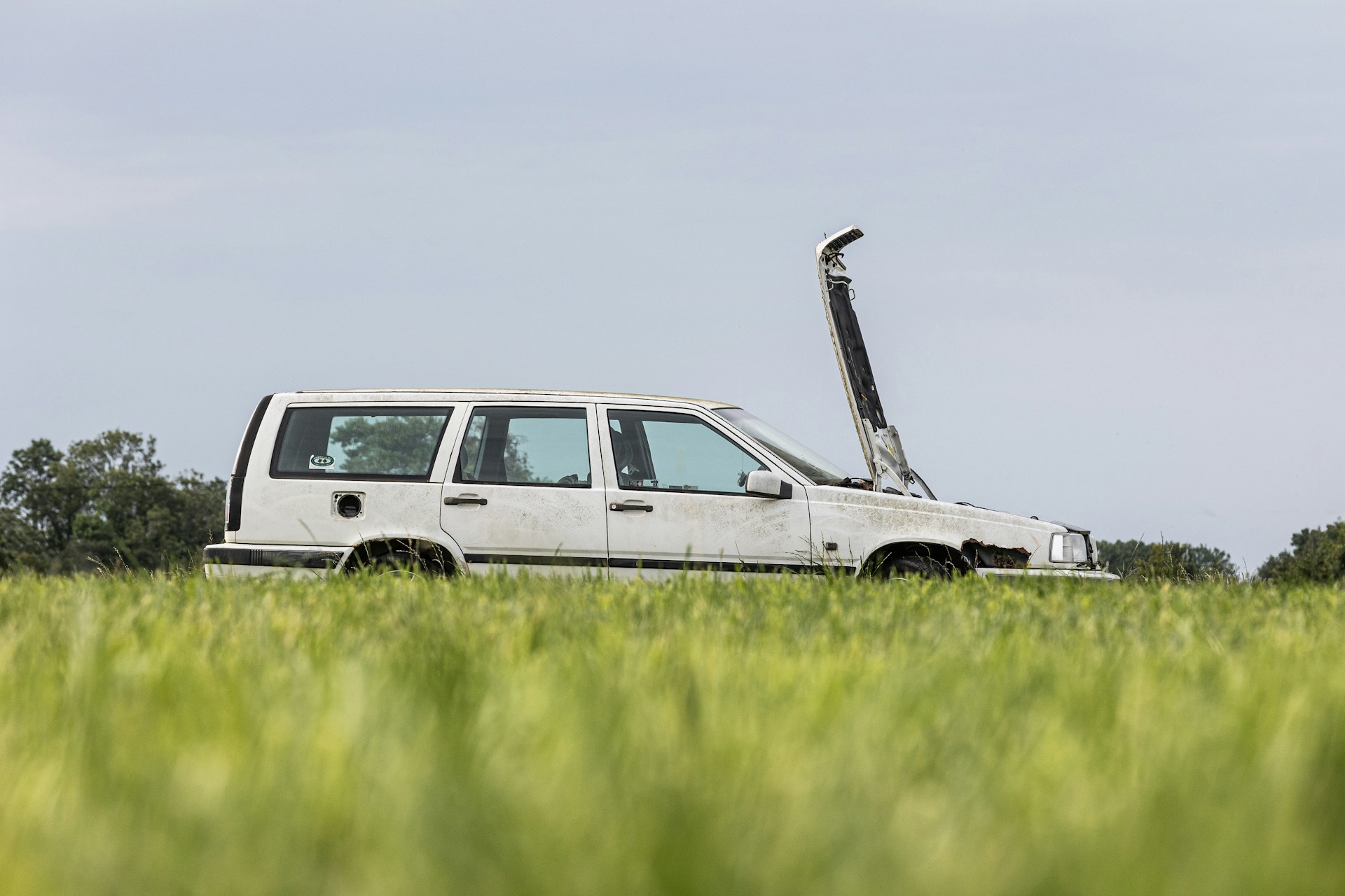 Old white car with an open hood standing in the grass