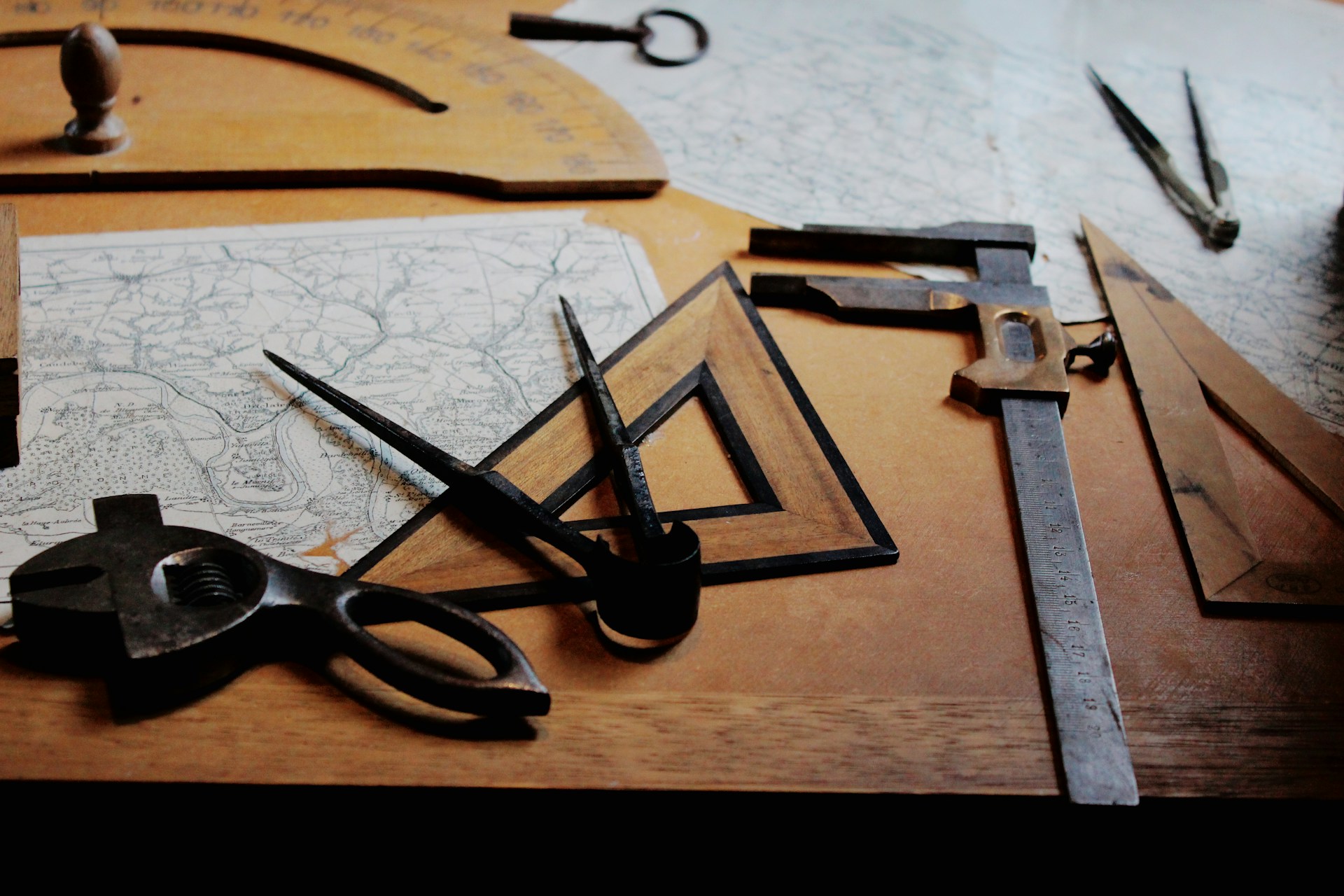 Historic drafting tools arranged across maps and technical plans on a wooden worktable.