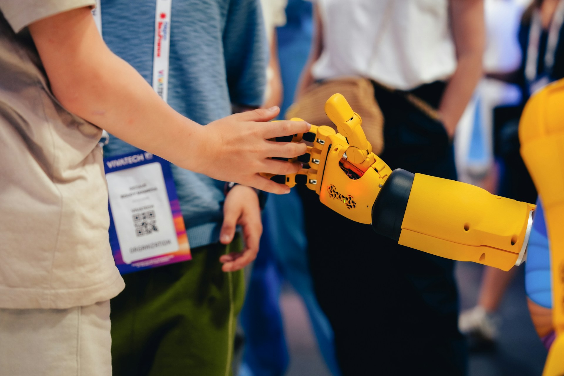 En person som berører hånden til en gul robot på et teknologisk arrangement, som representerer menneskelig kontroll over AI